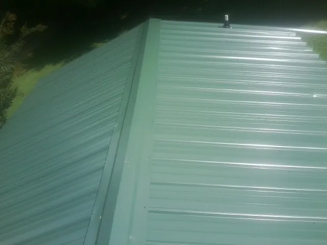 New green metal panels meeting at the ridge of a roof — Flat Roof Repair work by our crew in Lake Toxaway