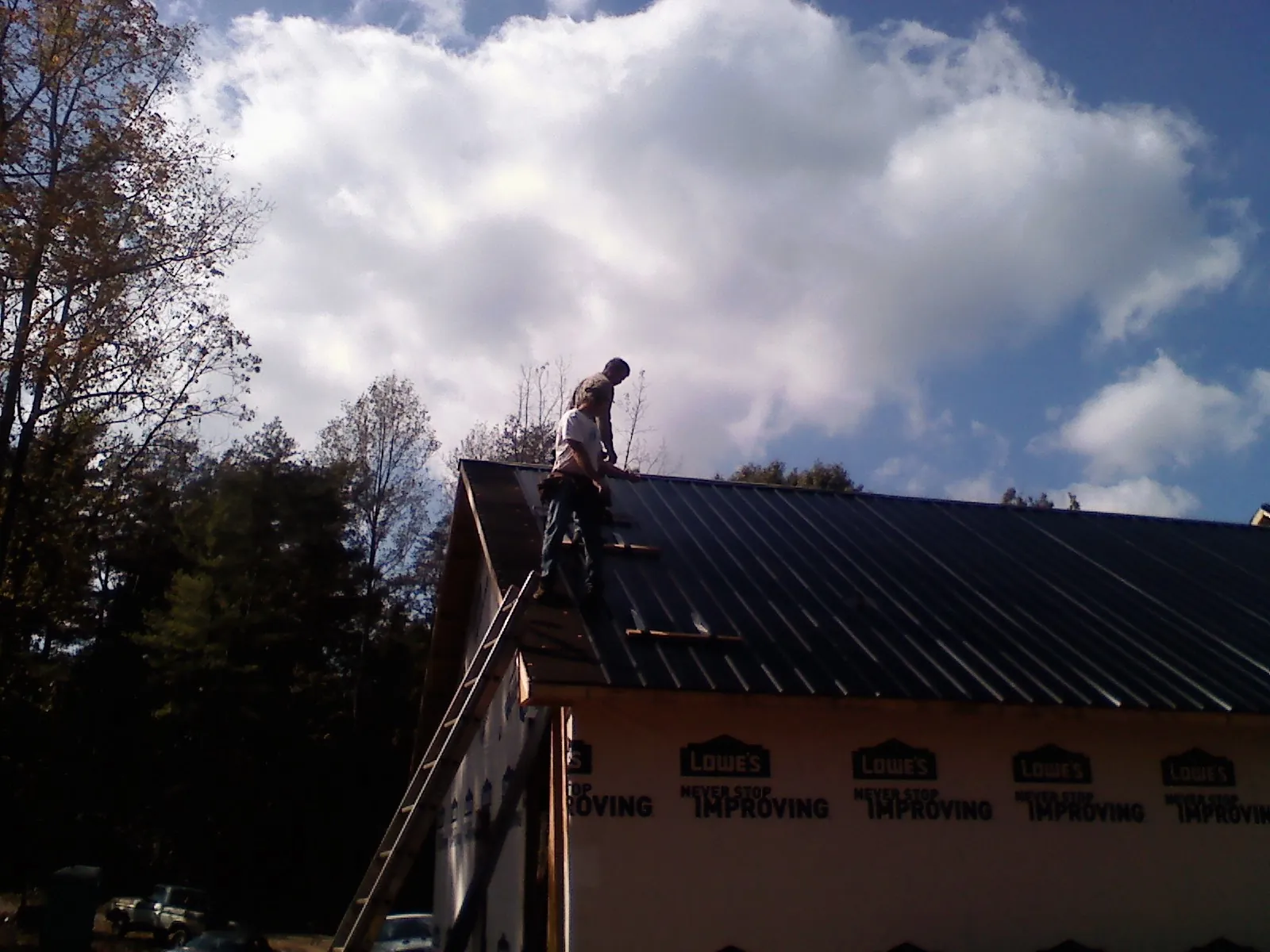 Roofer fastening dark metal panels high against a cloudy sky, from a Roof Inspection job in Lake Toxaway