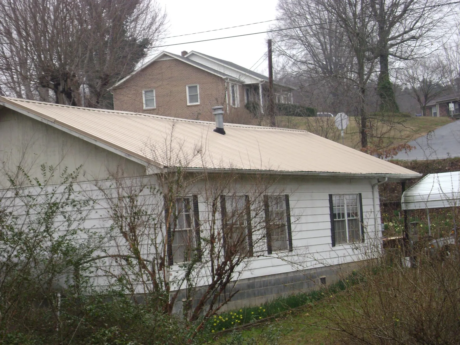 Tan metal roof on a white sided house set into a hillside — Commercial Roofing by Roofing Brothers in Lake Toxaway