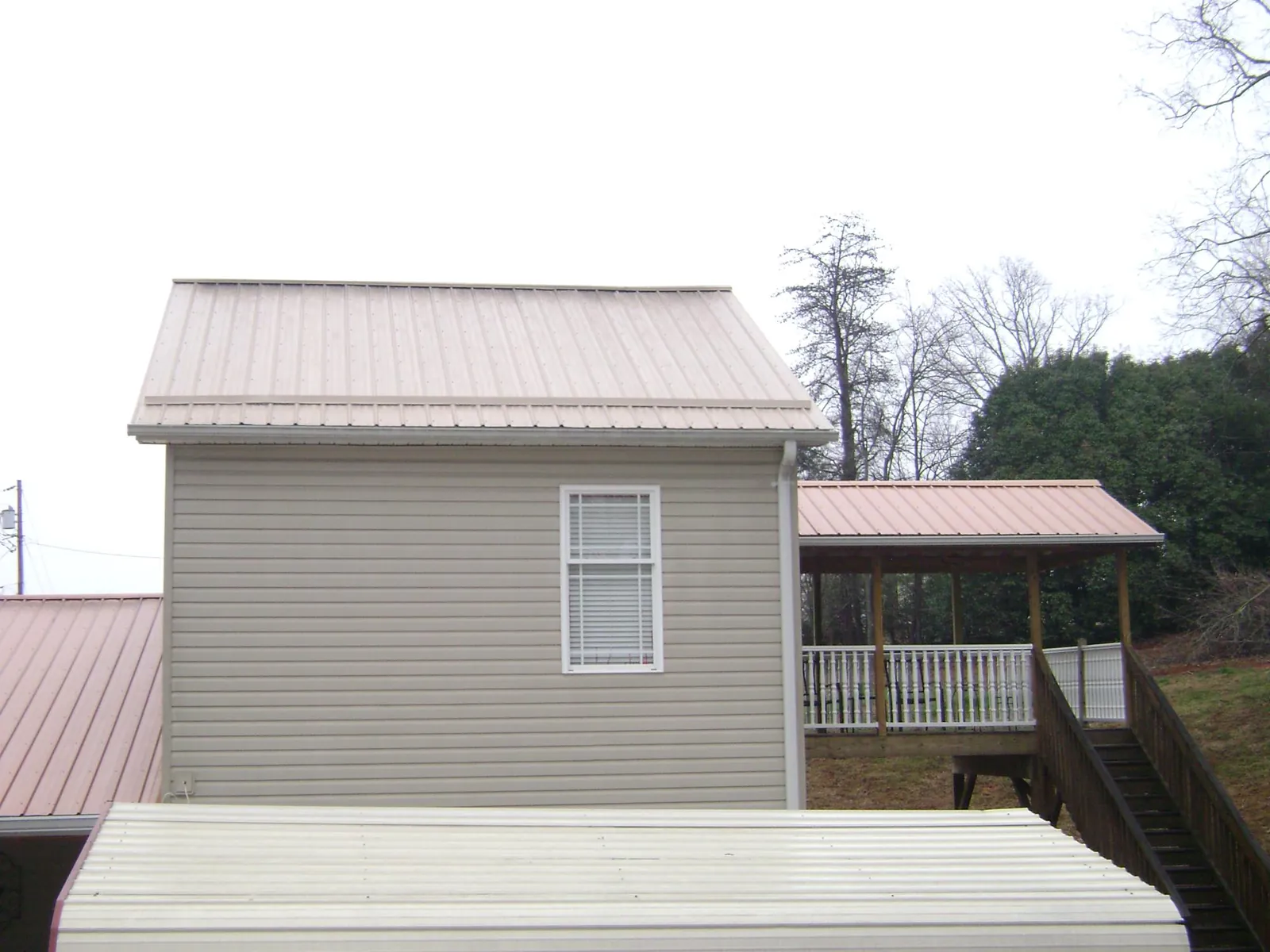 Tan metal roofs on a two story addition and attached porch, from a Roof Replacement job in Lake Toxaway